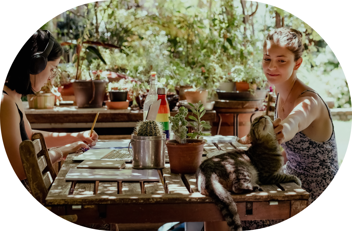 couple of woman drinking alcohol, one pours beer on a plastic cup, the other watches and smiles, they are sitting by the water, mountains in the background