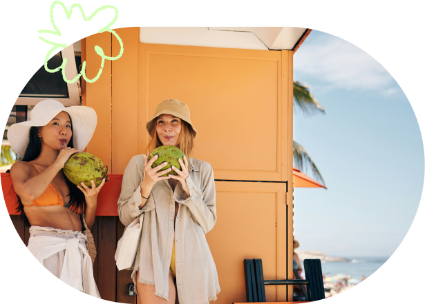 couple of woman drinking coconut water from coconuts with straws on the beach